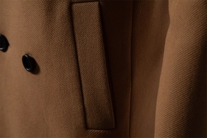Detailed close-up of textured twill wool coat featuring side pockets and black buttons