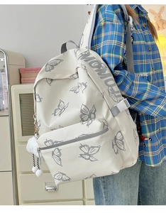 Side view of white butterfly print backpack with plush ball charm on a model