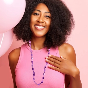Close-up of long purple beaded necklace with rectangular crystals on a pink background