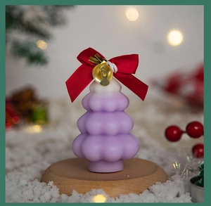 Macro shot of purple Christmas tree candle with white tip, red bow and golden bell