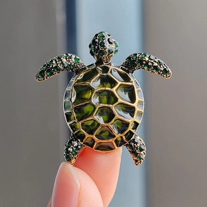 Macro shot of green enamel turtle brooch with gold hexagonal shell and crystal accents