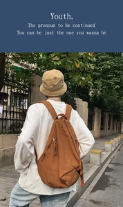 Brown washed canvas backpack featuring adjustable straps worn by a male in city streets