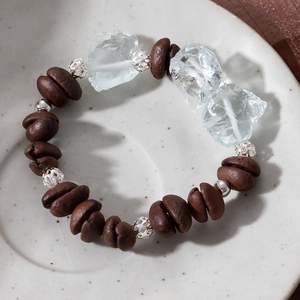 Close-up of coffee bean bracelet with silver hollow beads and blue crystal on ceramic tray