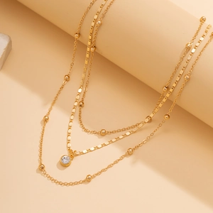 Macro shot of layered gold necklace with round beads and clear crystal pendant detail