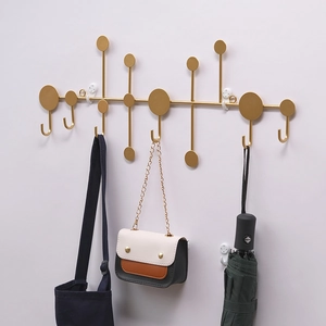 Wall-mounted golden metal coat rack with geometric hooks holding bags and umbrella
