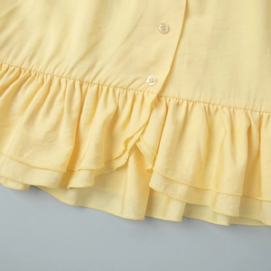 Detail of light yellow dress with tiered ruffle hem and white round buttons on the front
