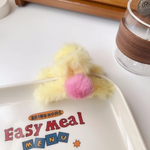 Detail of yellow plush hair claw with pink pompom displayed on a ceramic plate