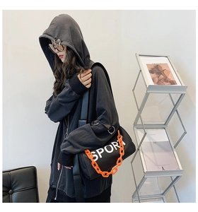 Détail du sweat à capuche gris à anneaux et sac cylindrique noir avec une chaîne orange vive