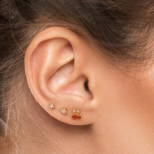 Close-up of golden 925 silver cartilage studs with crab and star shapes on a model's ear