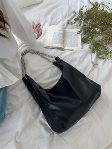 Detail of minimalist black PU leather tote bag with silver metal chain strap on white linen