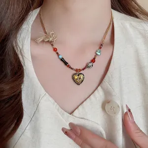 Vintage gold heart necklace with colorful beads and cross pattern on a white shirt