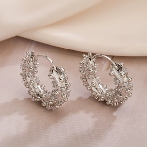 Pendientes de aro plateados con circonitas texturizadas sobre fondo elegante