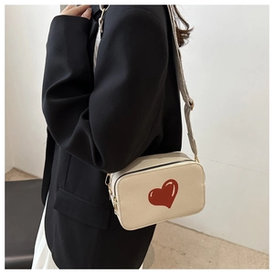 Detail of off-white crossbody bag with red heart and wide strap on model in black suit