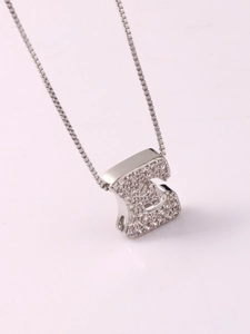 Detail of silver letter E pendant with inlaid zircons on a reflective surface