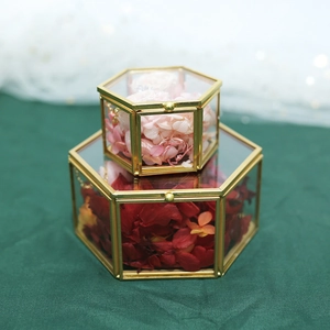 Stack of gold metal hexagonal glass ring boxes with dried flowers on green fabric