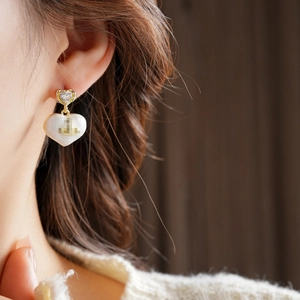 Detail of a gold-plated heart earring with white enamel and a Saturn charm on a model