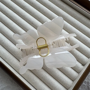 Close-up of translucent white butterfly hair claw clip with golden spring on velvet tray