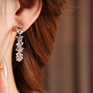 Macro view of C-shaped silver needle earrings featuring sparkling zircon stars on ear