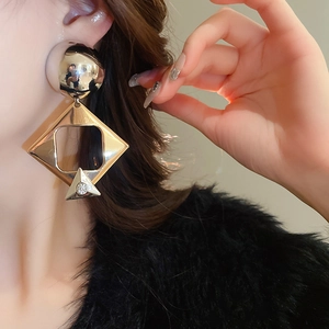 Close-up of gold geometric drop earrings with sparkling diamonds on a female model