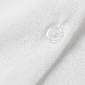 Macro shot of white crepe fabric texture and a four-hole button on the shirt placket