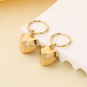 Golden heart pendant earrings displayed on a white podium with silk texture background
