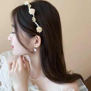 Détail d'un serre-tête fleuri avec roses crème, feuilles dorées et perles sur modèle