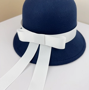 Detailed close-up of a navy blue wool felt academy style cloche hat with a white ribbon bow