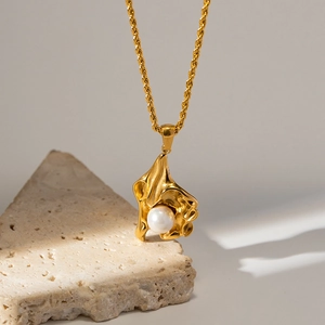 Detailansicht der goldenen Kordelkette und des künstlerischen Perlenanhängers auf Stein