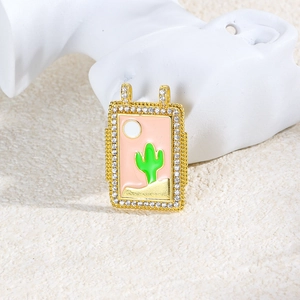 Close-up of rectangular gold pendant with pink enamel desert scene and inlaid gems