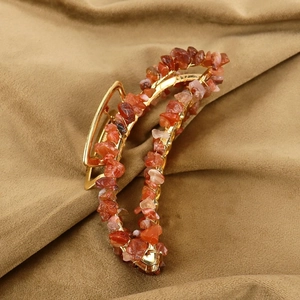 Close-up of handmade gold metal hair claw with red natural stone chips on brown fabric