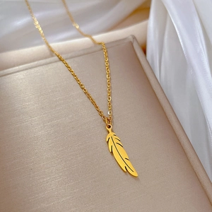 Gros plan détaillé d'un collier avec pendentif plume dorée sur un tissu en soie blanche