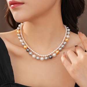 Détail d'un collier de perles à double rangée blanche et dorée porté par un mannequin
