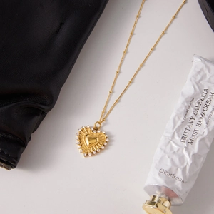 Detailed shot of 18K gold heart pendant with radiating design and rhinestone edges