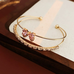 Detail view of double-layer golden bangle with pink crystal butterfly and zircon stones