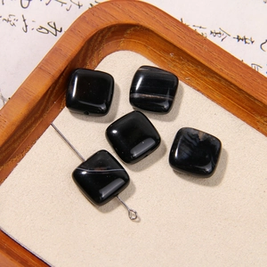 Macro detail of square black natural stone beads with white veins on a beige pad