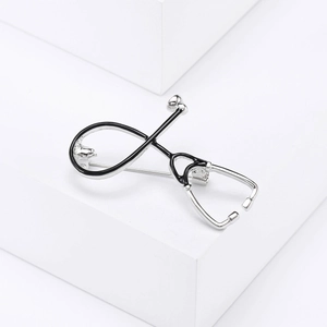 Detail of silver stethoscope brooch with black enamel inlay on white background