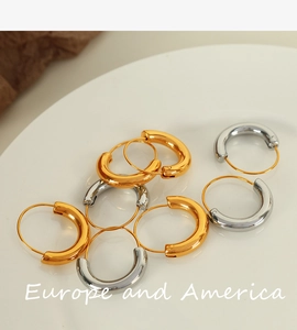 Detailed close-up of chunky gold and silver geometric hoop earrings in a white ceramic dish