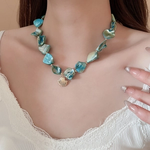 Detail of teal seashell necklace with a golden shell pendant on a model neck