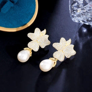 Close-up of gold flower earrings with zircon pavé and teardrop pearl drops on black background