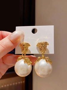 Dettaglio di orecchini vintage dorati con emblema Medusa e grandi perle pendenti