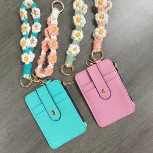 Flat lay of pink and mint leather card holders with braided floral lanyards on wood surface