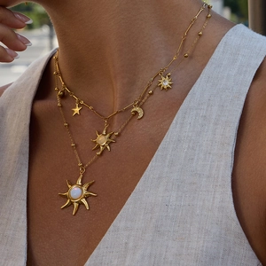 Primo piano di collane a strati in acciaio inox oro 18K con ciondoli sole, luna e stella