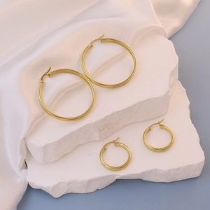 Detail of gold flat round hoop earrings in two sizes on a white marble display stand