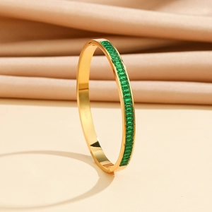 Detail view of gold stainless steel bangle with emerald green baguette zircons
