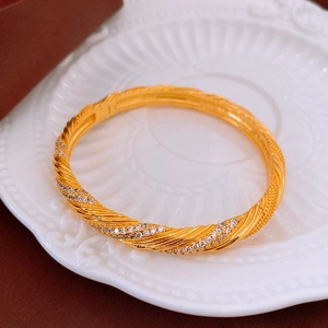 Close-up of gold plated twisted vintage bangle with sparkling zircon stones in a ceramic tray