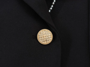 Détail d'un bouton métallique doré avec motif texturé complexe sur une robe noire