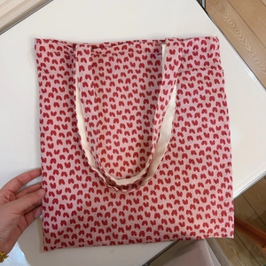 Detailed flat lay of pink canvas tote bag with red floral patterns and white handles