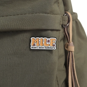 Detail of MILF Man I Love Folklore enamel pin on a dark green backpack strap