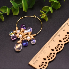 Detail of gold hoop earrings with purple glass droplets and freshwater pearls next to a ruler