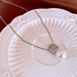 Détail d'un collier argenté avec pendentif en zircon et perle sur une assiette blanche
